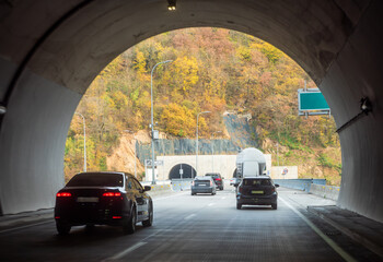 Fototapeta premium Cars driving through mountain tunnels in autumn, highway traffic in scenic landscape, road infrastructure in hilly terrain.