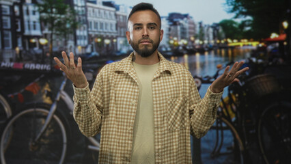 Man gesturing with hands on street by amsterdam canal with bicycles and buildings visible;...