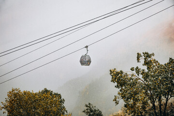 Gondola cabins move across the foggy Dombay sky during an early snow, showcasing the contrast between golden autumn foliage and harsh mountain weather © inna717