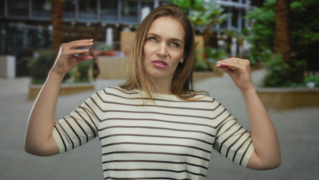 Young caucasian woman using expressive hand gestures while speaking in a city street setting; communication. - Powered by Adobe