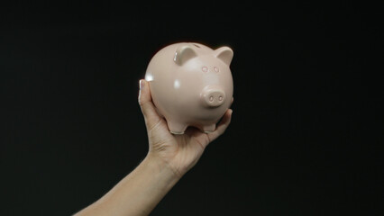Hand holding pink piggy bank against black background, representing savings and financial security,...
