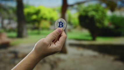 Man holding bitcoin outdoors with green park scenery in background highlighting cryptocurrency in nature