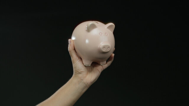 Hand holding pink piggy bank against black background, representing savings and financial security, ideal for investment concepts featuring isolated objects.