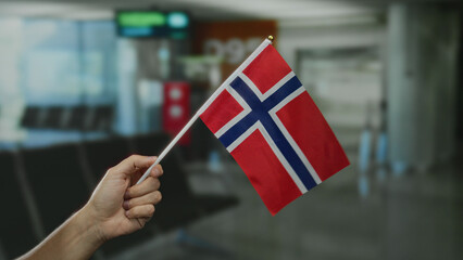 Hand holding norwegian flag in an airport terminal, showcasing a patriotic gesture indoors.