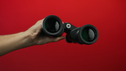 Man holding binoculars against a vibrant red background, highlighting the focus on exploration,...