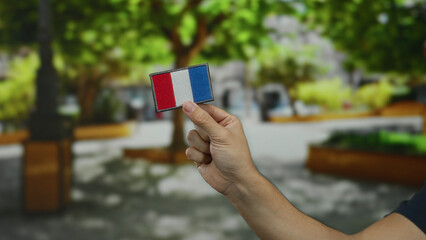 Man holding an embroidered french flag patch in a park, showcasing national pride amidst lush greenery and outdoor ambiance.
