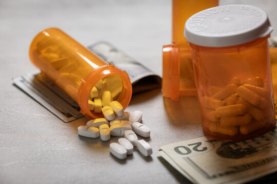 A visually impactful shot featuring prescription pill bottles and scattered US dollar bills (cash). This image symbolizes the high cost and financial burden of medication and the debt caused by health - Powered by Adobe