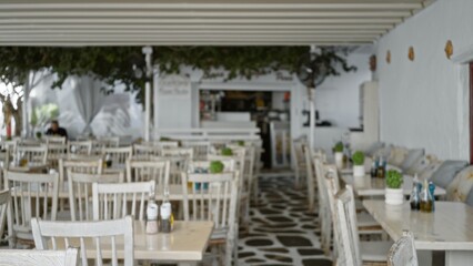 Whitewashed open cafe with rows of rustic wooden tables and chairs in soft blurred bokeh, shallow focus; background backdrop copyspace calm.