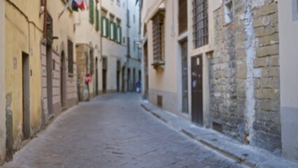 Fototapeta premium Narrow cobblestone alley defocused bokeh with soft focus on textured stone and stucco facades, receding urban passage and muted warm tones; background backplate copyspace calm.