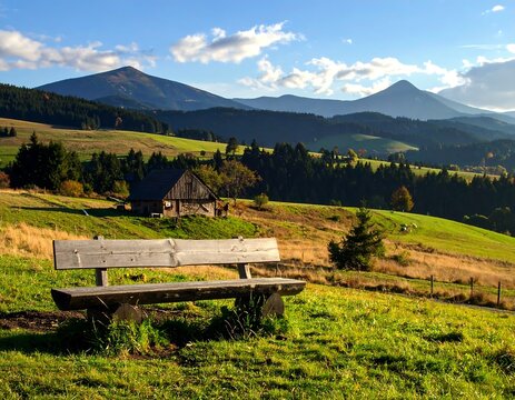 A wooden bench sits atop a grassy hill overlooking a vast rural landscape with rolling green fields and distant mountains