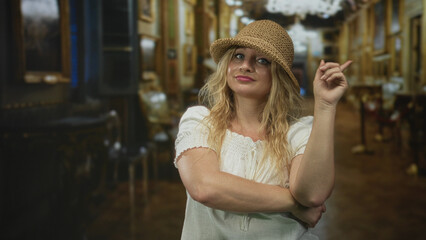 Woman in straw hat and white blouse with crossed arms points finger inside building while looking...