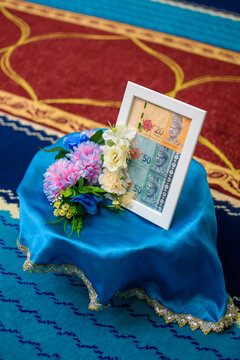 A framed display of Malaysian Ringgit currency presented on a blue satin cushion with flowers as a traditional dowry