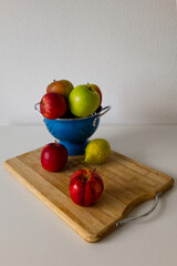 Fresh apples and pears in a blue colander on a wooden board in the kitchen. Colorful assortment of fresh fruits. Healthy eating, cooking, local and sustainable consuming, and grocery concepts.