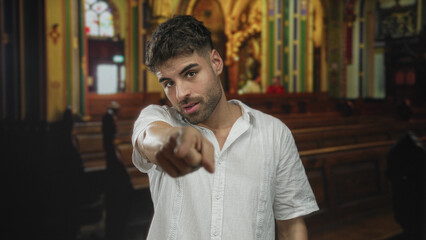 Man in white shirt points finger in building aisle at camera with serious expression; stern moral...