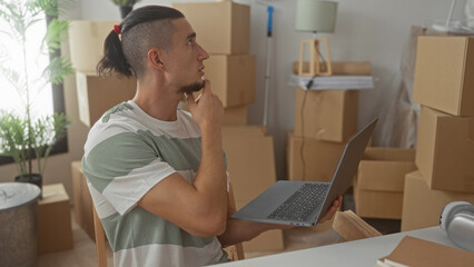 Man holding laptop and pointing finger amid stacked moving boxes in a building living room of a new home; focused planning.