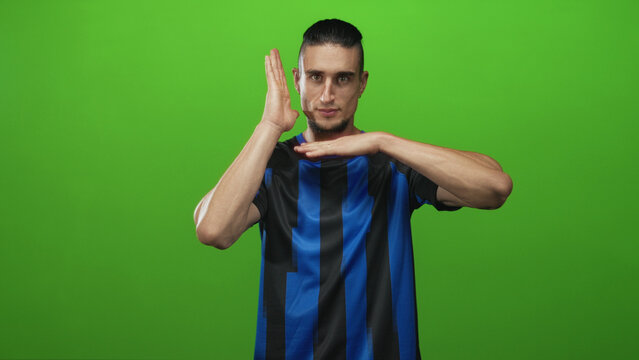 Man in blue and black soccer jersey with hands forming a t time out gesture in green screen studio; determination teamwork.