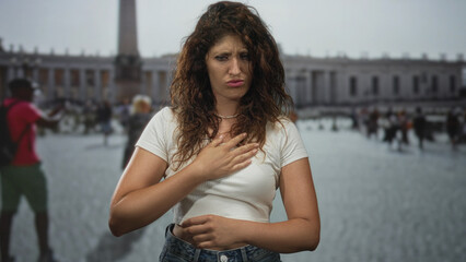 Fototapeta premium Woman clutching chest with hand suggesting heartattack on street at st peter's square, vatican; distress emergency.