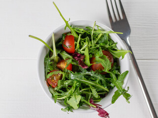 Fresh Arugula Salad with Cherry Tomatoes in White Bowl on Wooden Table
