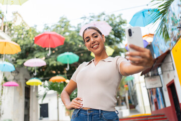 Happy latina woman taking a selfie on a street decorated with colorful umbrellas