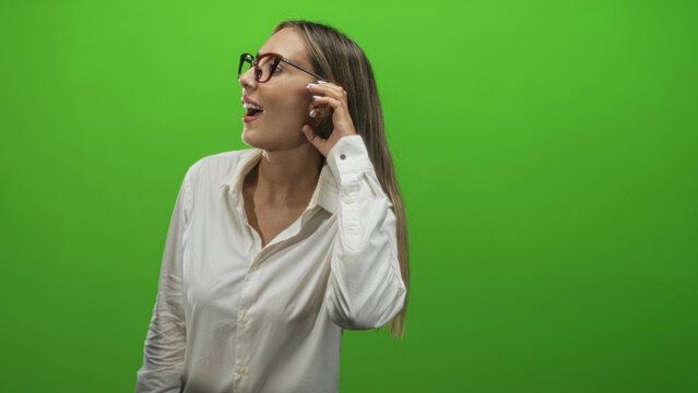 Woman with glasses holding hand to ear in green studio, gazing to the side as if listening intently; curiosity. - Powered by Adobe