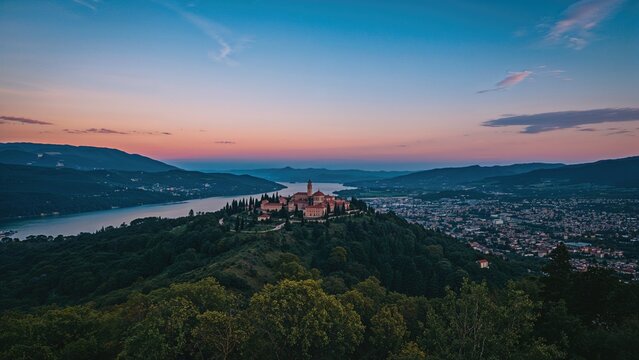A view of a historic castle on a hilltop overlooking a lake and cityscape at sunset.