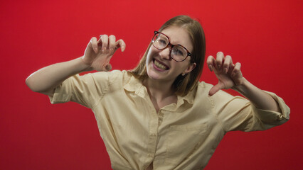 Woman making claw gesture with raised hands and smiling in red studio; playfulness joy fun amusement.