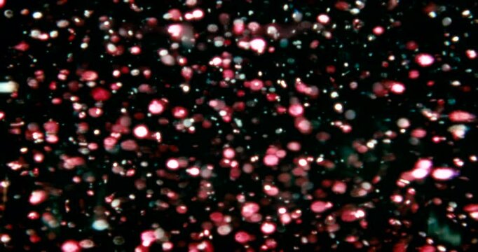 Red, blue, and silver particles drift through water in a dark space, reflecting cool and warm light&mdash;cosmic, dreamy, glittering star-like movement.