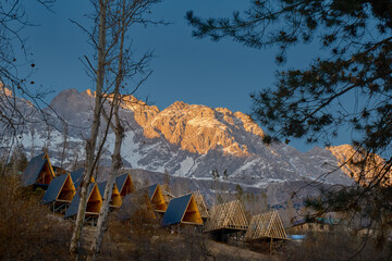 A-frame cabins on snowy hillside at sunrise, under construction, forest retreat with mountain view.