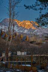 A-frame cabins on snowy hillside at sunrise, under construction, forest retreat with mountain view.