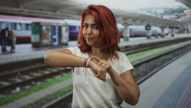 Woman checking watch on wrist at train station building platform, rings and bracelets visible; impatience commute hurry.