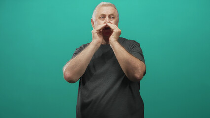 Senior man cupping hands to mouth shouting in studio with teal wall, visible bare hands and forearms in profile calling out to distance; communication urgency.