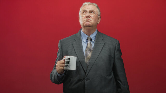 Man holding mug reading 'i am the boss', chin raised and stern expression, gaze upward in studio; authority leadership pride.
