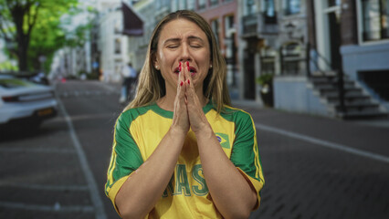 Woman in yellow jersey rubs fists against her eyes on street; sadness disappointment longing reflection.