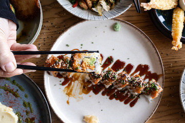 Hand picking a sushi roll with chopsticks from a plate