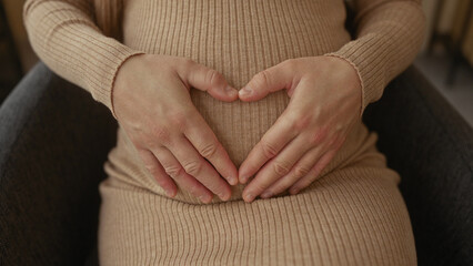 Pregnant woman in beige dress cradling her belly while sitting indoors in a cozy office, emphasizing maternal anticipation in a serene workplace setting.