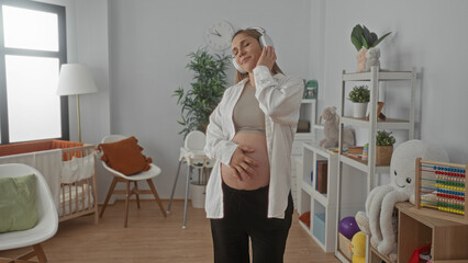 Pregnant woman enjoying music with headphones in cozy baby room surrounded by toys and crib