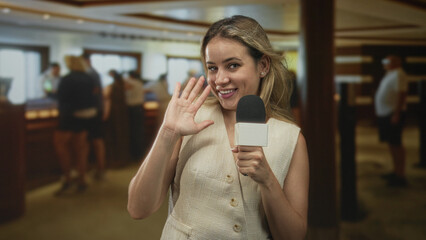 Woman reporter holding microphone and waving hand in building hotel lobby reception; confident friendly.