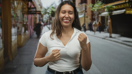 Woman with fists raised on a busy city street, smiling with closed eyes; joy celebration resilience.