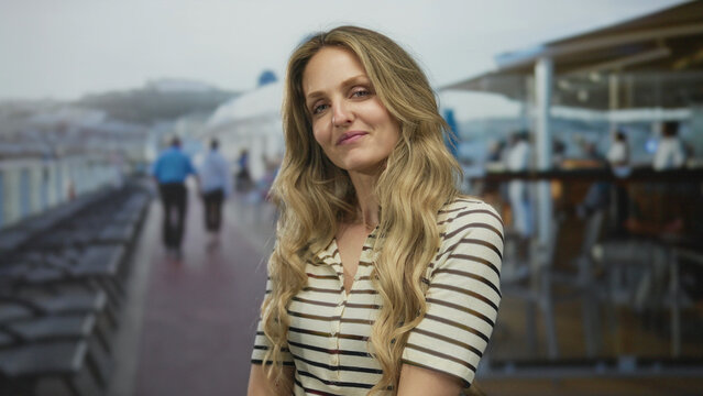Confident woman shows flowing hair while smiling on a boat, young blonde traveler enjoying a cruise from an outdoor deck overlooking ocean.