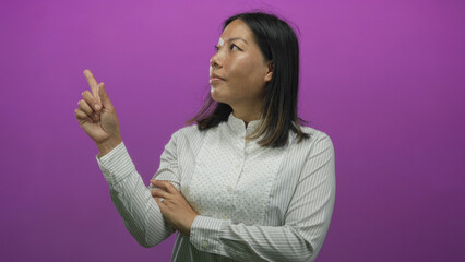 Woman points index finger upward in purple studio with crossed arm and white striped shirt; confidence focus.