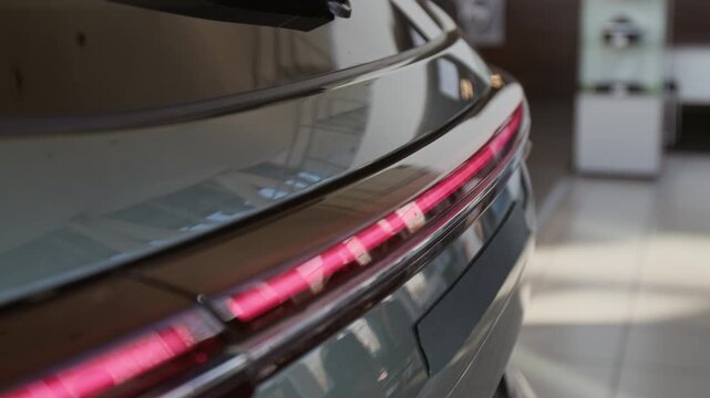 Close up detail shot of full width red light neon strip on sleek modern car reflecting light on display in car dealership, copy space