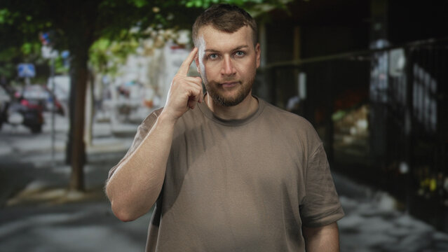 Man points finger at camera on street while touching temple with index finger in accusatory gesture; direct challenge confidence.