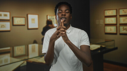 Man gives pistol gesture with bent fingers and points finger toward camera in building interior;...