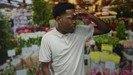 Young african american man shields eyes over fresh pink tulip bouquets on street; curiosity exploration.