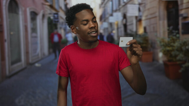 Man grips creditcard with right hand on busy urban street outdoors next to historic building facade; confidence. - Powered by Adobe