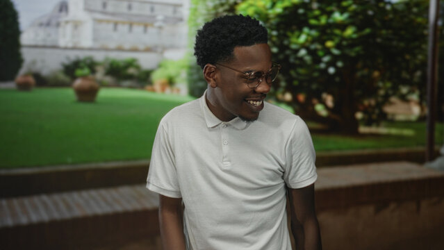 Man wearing white polo smiles showing mouth in sunny building courtyard with potted plants; joyful connection. - Powered by Adobe