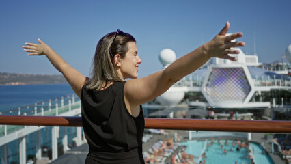 Woman standing with outstretched arms and hands on railing on cruise deck overlooking pool and sea; serenity travel escape.