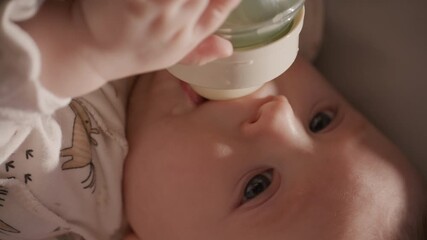 Lovely baby being held by parent, drinking milk from bottle during feeding routine at home. Vertical close-up shot - Powered by Adobe