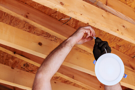 Electrician is fixing lighting fixture to ceiling in home renovation setting, on details safety. - Powered by Adobe
