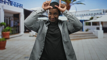 Man showing hands in pointing and l shaped gesture to head while standing before a modern building...
